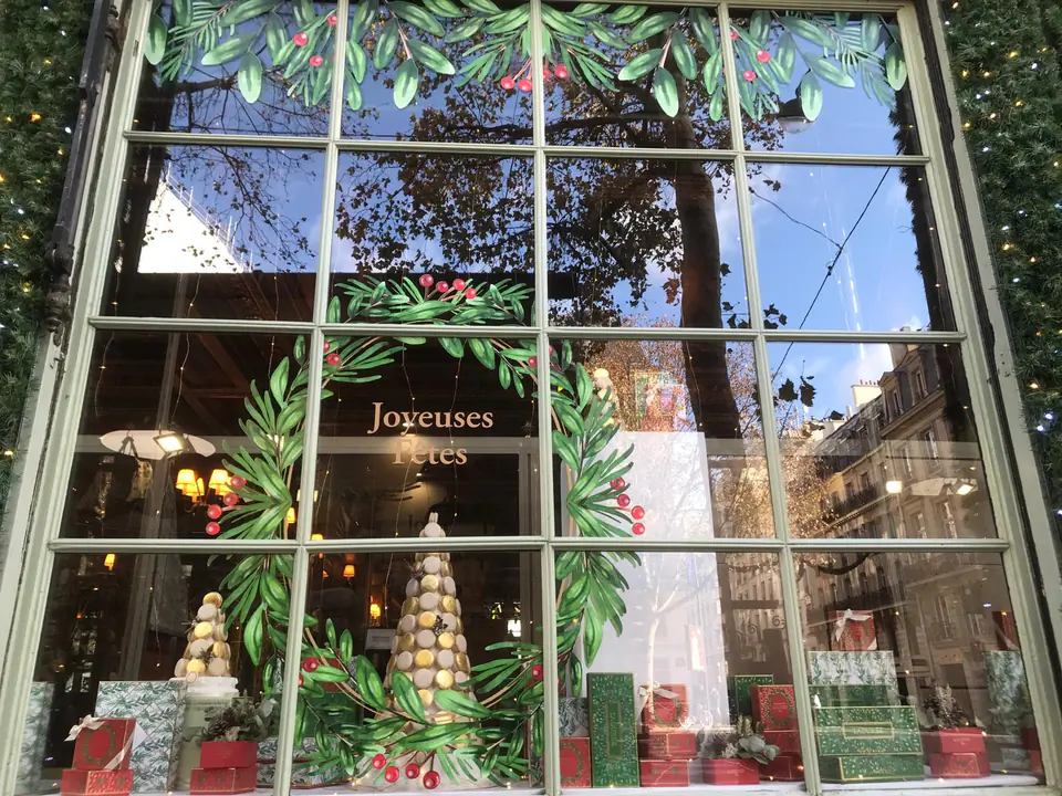 Vitrine de Noël Ladurée entourée de guirlandes lumineuses, couronne de feuillage en vitrophanie au centre