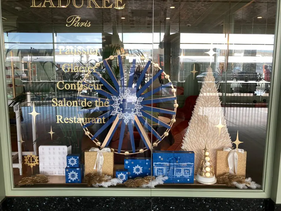 Vitrine d'hiver Ladurée : étoile bleue, flocon et lettrage doré sur le vitrage, sapin blanc et coffrets bleus