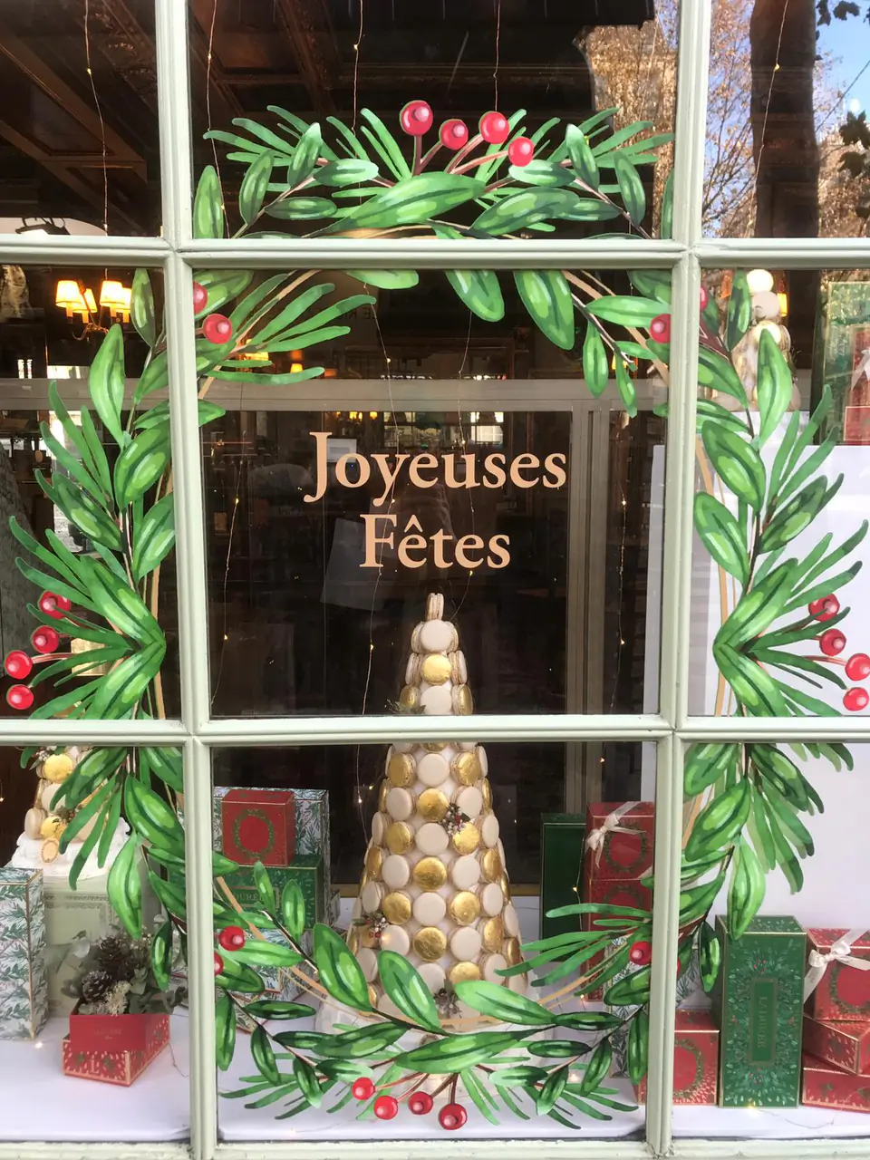 Vitrophanie de Noël Ladurée vue de près : couronne d'olivier et baies rouges encadrant une pyramide de macarons